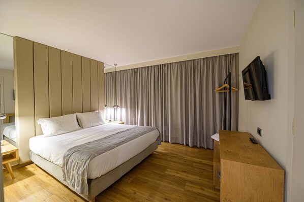 Una habitación de hotel moderna con una cama grande, suelo de madera, televisor y armario.