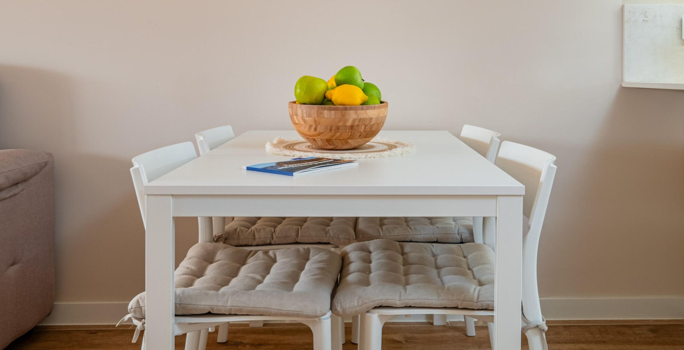 Een eettafel met een houten schaal vol fruit, een tijdschrift en comfortabele stoelen.