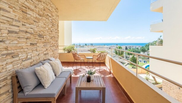 A balcony with a stone wall, a sofa, two chairs, and a table.