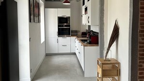Eine schmale Küche mit weißen Schränken, einem roten Wasserkocher und einem Holztisch.