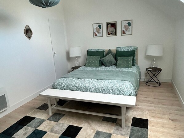 Un dormitorio con una cama, dos mesitas de noche, un banco, un tapete estampado y tres cuadros en la pared.