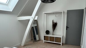 Ein Schlafzimmer im Loft-Stil mit schrägem Dach, einem weißen Bett, einem kleinen weißen Konsolentisch mit Dekoration und einer grauen Tür sowie Holzdielen.