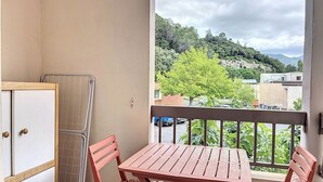 A balcony with a table and chairs, a radiator, and a view of a green landscape with trees and buildings.