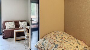 A room with a bed, a chair, a small table, and a door.