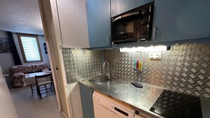A compact kitchen with a microwave, sink, and dishwasher. A dining area with a couch and table is visible in the background. - Divisible studio, southwest balcony, quiet, 24m² (La Plagne Montchavin Les Coches)
