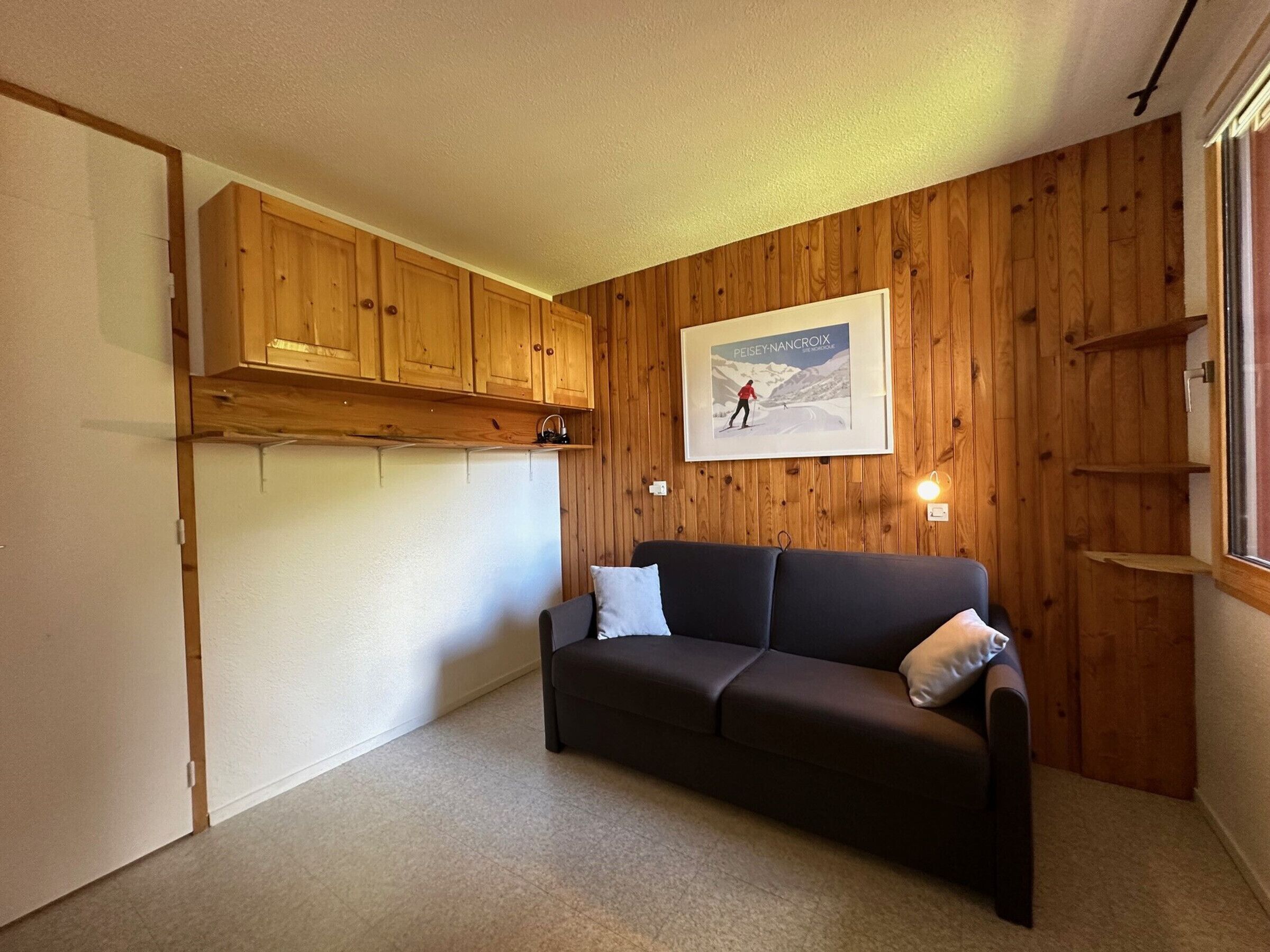 A cozy room with a wooden wall, a framed picture, a dark sofa, and a small shelf.