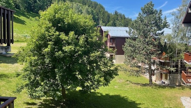 A mountain lodge with a large tree in the foreground, a wooden deck, and a view of the surrounding forest and hills. - Divisible studio, southwest balcony, quiet, 24m² (La Plagne Montchavin Les Coches)