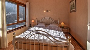 A bedroom with a wooden ceiling, a bed with white bedding, two bedside tables with lamps, a window with curtains, and a framed picture on the wall.