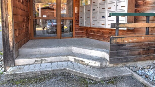 A wooden cabin with a glass door entrance, a mailbox, and a stone-paved porch.