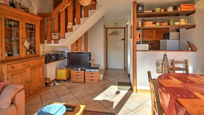 A cozy living room with a wooden staircase, a television, and a dining area with a table and chairs.