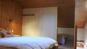Puinen huone, jossa on sänky, seinään kiinnitetty valaisin ja kattovalokuvio.