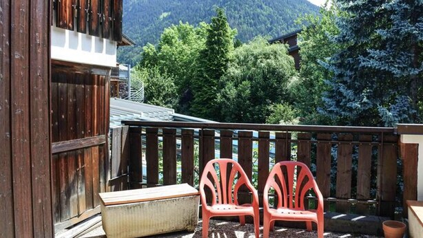 A balcony with two red chairs, a wooden table, and a view of a mountain. - Morzine: Cozy mezzanine studio for 6, city center (Morzine)