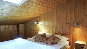 A wooden-paneled bedroom with a bed, pillows, and bedside tables. - Morzine: Cozy mezzanine studio for 6, city center (Morzine)