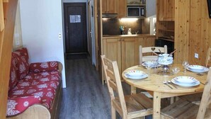 A compact kitchen with wooden cabinets, a microwave, and a dining area with a round table and chairs. - Morzine: Cozy mezzanine studio for 6, city center (Morzine)