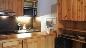 A kitchen with wooden cabinets, a microwave, a sink, and a rack with kitchen utensils. - Morzine: Cozy mezzanine studio for 6, city center (Morzine)