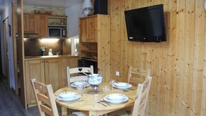 A wooden-paneled dining area with a round table set for four, equipped with plates, glasses, and cutlery. A television is mounted on the wall above the table. - Morzine: Cozy mezzanine studio for 6, city center (Morzine)