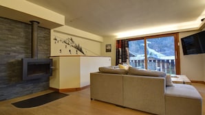 A living room with a stone fireplace, a sofa, and a large window with a view of a snowy landscape. - Chalet in Morzine for 10 people, parking, wifi (Morzine)