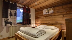 A wooden-paneled room with a bed, a window with curtains, a radiator, and a painting on the wall. - Chalet in Morzine for 10 people, parking, wifi (Morzine)
