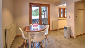 A dining area with a round table and four chairs, a radiator, a trash bin, and a window with a view of greenery. - Chalet in Morzine for 10 people, parking, wifi (Morzine)
