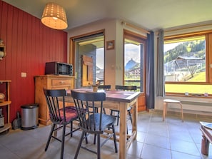 A cozy kitchen with a dining table, chairs, and a microwave. There is a window with a view of a mountain and buildings.
