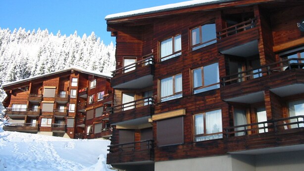 Un edificio de madera de varios pisos con balcones, rodeado de árboles cubiertos de nieve.