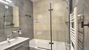Un baño moderno con ducha envuelta en vidrio, una bañera blanca y un tocador con espejo.