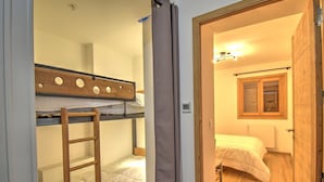 Una habitación con literas, una escalera, una ventana con cortinas y una puerta que da a otra habitación.