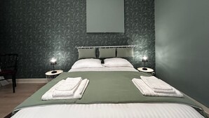 Un lit bien fait, avec des oreillers et des serviettes pliées, deux tables de chevet avec des lampes, une chaise et un papier peint à motifs.