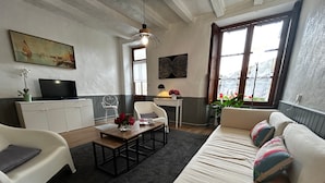 Un salon avec un canapé, une table basse ornée de fleurs, un téléviseur et un tableau accroché au mur.
