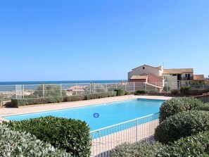 A swimming pool with a clear view of the sea, surrounded by a fence and greenery. - Cozy 2-Room Apartment with Pool, Tennis, and Parking Near Beach - Sleeps 6 (Fleury-Saint-Pierre-la-Mer)