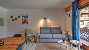 Ein modernes Wohnzimmer mit einer grauen Couch, einem Holzesstisch und einem kleinen runden Tisch mit einer Pflanze.