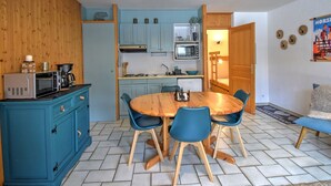 Eine kleine Küche mit blauen Schränken, einem Holztisch mit vier Stühlen und einer Mikrowelle.