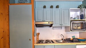Eine kleine Küche mit Herd, Backofen und Spüle. Schränke und eine Arbeitsplatte sind vorhanden.