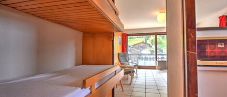 Una habitación con una cama litera, una silla, una mesita y vistas a una casa a través de un ventanal.