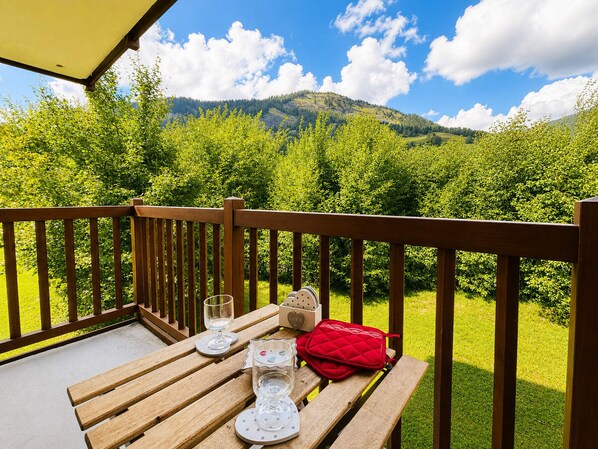 A wooden deck with a table set for two, overlooking a lush green landscape with mountains in the distance.