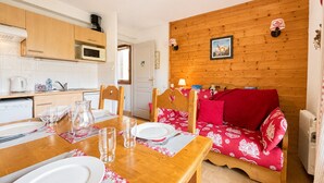 Une pièce chaleureuse avec un mur en bois, une table à manger dressée pour deux personnes et un canapé rouge.