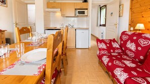 Un espace de vie compact comprenant un coin repas, une kitchenette et un canapé rouge à motifs.