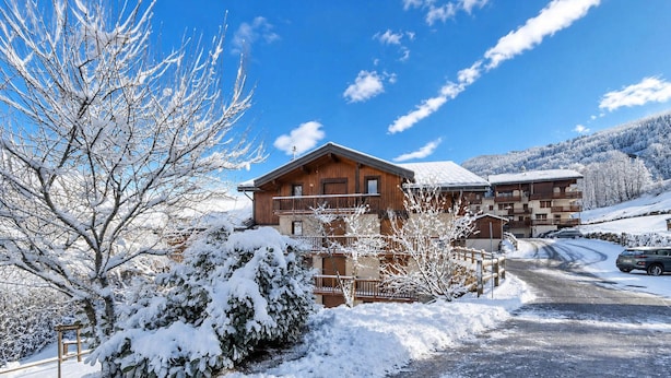 Een houten chalet met balkon, omringd door met sneeuw bedekte bomen en een heldere lucht.