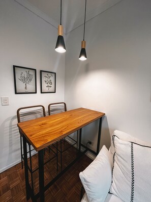 Un comedor con una mesa y sillas de madera, dos lámparas colgantes y dos láminas botánicas enmarcadas en la pared.