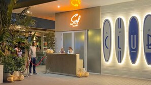 Un edificio moderno con una recepción, un letrero de neón que dice "Surf Club" y varios botes de surf iluminados en la pared.