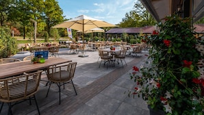 An outdoor patio area with multiple tables and chairs, surrounded by greenery and trees. - Wooden Lodge Near Three National Parks (Ruinen)