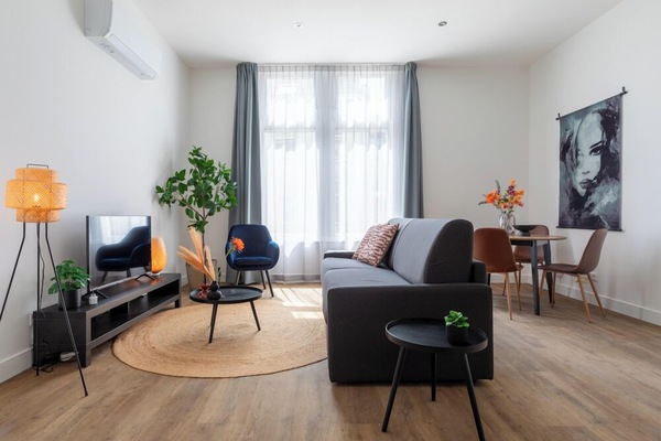 A contemporary living area with a plush sofa, chic chairs, sleek round tables, a TV unit, and natural accents, all enhanced by warm hues and lush greenery, seamlessly linking to the dining space.
Apart-Hotel – close to the university, city center, Efteling & Safaripark Beekse Bergen. Equipped with a new kitchen and a luxury bathroom.