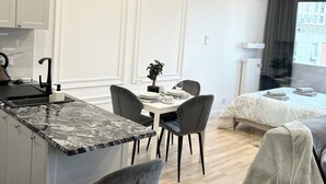 Una cocina moderna con encimera de mármol, un comedor con mesa y sillas, y un dormitorio con cama y ventana.