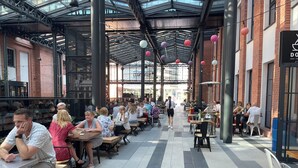 Un espacio de comedor al aire libre con mesas y sillas, un paseo cubierto y un edificio con un letrero que dice "DO".