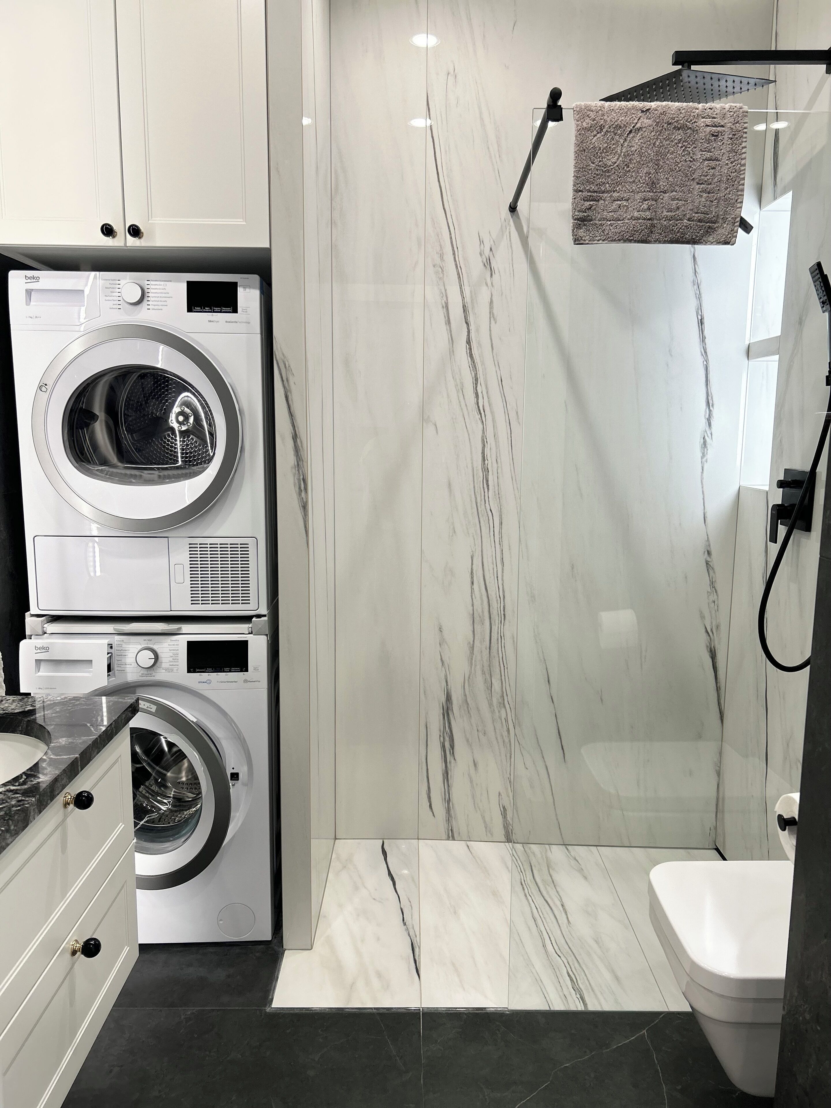 A modern bathroom with a built-in washer and dryer, a glass shower enclosure, and a toilet.