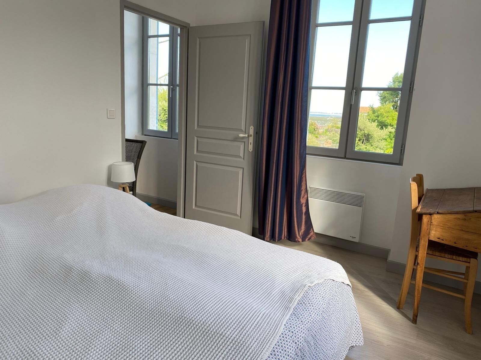Une chambre à coucher avec un lit, une chaise, un bureau et une fenêtre avec des rideaux.