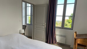 Ein Schlafzimmer mit einem Bett, einem Sessel, einem Schreibtisch und einem Fenster mit Vorhängen.
