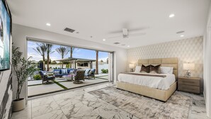 Une chambre moderne avec un grand lit, un ventilateur de plafond et une vue sur la terrasse extérieure.