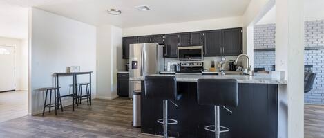 A modern kitchen with dark cabinets, stainless steel appliances, and a central island with bar stools.