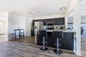 A modern kitchen with dark cabinets, stainless steel appliances, and a central island with bar stools. - Cozy 3BR House Near Attractions & Shopping (Phoenix)